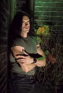 Peter Steele leaning against a green-lit brick wall at night, arms crossed