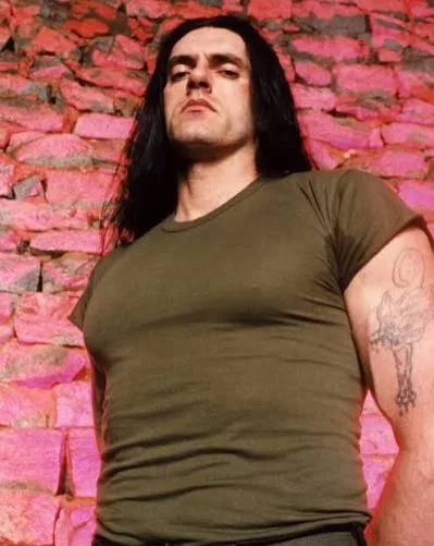 Peter Steele photographed from a low angle against a pink stone wall during the 1990s