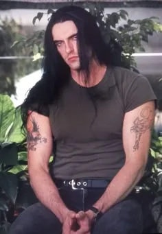 Peter Steele seated outdoors among plants, tattooed arms and long black hair